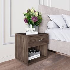 a nightstand with books and flowers on it next to a bed