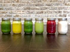 five jars filled with different colored liquids sitting on a wooden table next to a brick wall