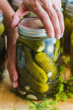 pickled cucumbers in a jar being held by a woman's hand