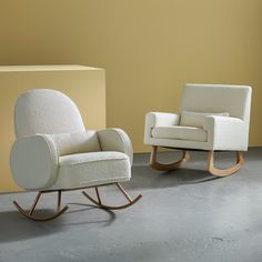 two white rocking chairs sitting next to each other on a cement floor in front of a yellow wall