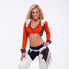 a woman in an orange top and white pants posing for the camera with her hands on her hips