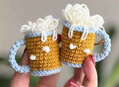 two crocheted coffee mugs are held up in the palm of a hand