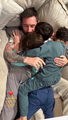 a group of people hugging each other on a bed with pillows and blankets behind them