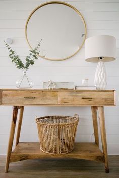 a wooden table topped with a basket under a mirror next to a wall mounted round mirror