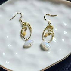 Indulge in the celestial allure of these captivating enchanted evening moonstone earrings. Crafted with precision and passion, each pair features 14k gold filled ear wire elegantly intertwined with 14k gold-filled wire, showcasing artisanal craftsmanship at its finest. Suspended delicately from these hooks are enchanting accents: a petite moonstone cloud pendant and a mesmerizing mother of pearl charm, evoking a sense of ethereal beauty and spiritual resonance. Radiating with love and meticulously handcrafted, these earrings are more than adornments--they are exquisite embodiments of magic and individuality. Embrace your inner goddess and elevate your style with these divine treasures. Mother of Pearl is cherished for its gentle yet powerful energy, which promotes emotional healing, protec Hypoallergenic Gold Moonstone Jewelry, Ethereal Moonstone Jewelry For Gift, Ethereal Oval Moonstone Jewelry, Ethereal Moonstone Gemstone Jewelry, Handmade Ethereal Dangle Earrings, Elegant Gold Crystal Earrings With Moonstone, Gold Moonstone Crystal Earrings As A Gift, Handmade Yellow Gold Moonstone Earrings, Gold Dangle Earrings With Moonstone