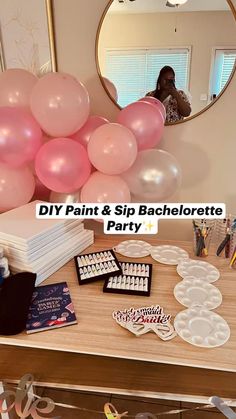 a table topped with lots of balloons and cake pans next to a mirror that says diy paint & sip bachelorette party