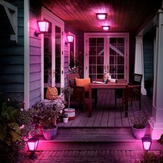 an outdoor patio with purple lighting and potted plants on the side walk, next to a wooden deck