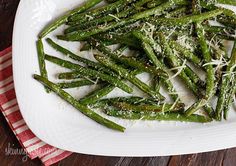 asparagus with parmesan cheese on a white platter next to a red and white checkered napkin