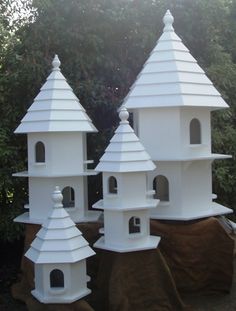 three large white bird houses sitting on top of a tree stump in front of some trees