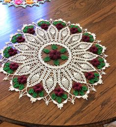 crocheted doily with red and green flowers sitting on top of a wooden table