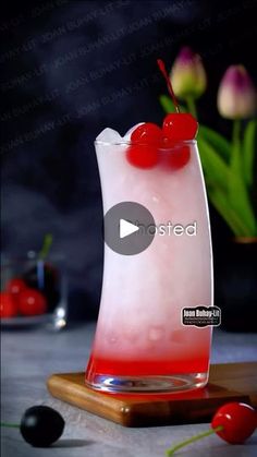 a red and white drink sitting on top of a wooden table next to some flowers