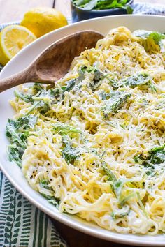 a white bowl filled with pasta and spinach on top of a table next to lemons