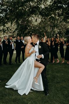 a bride and groom kissing in front of a large group of people wearing tuxedos