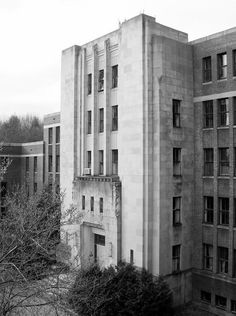 black and white photograph of an old building with trees in the foreground on a cloudy day