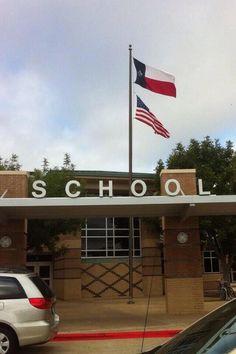 an american flag flying in front of a school building with cars parked on the street