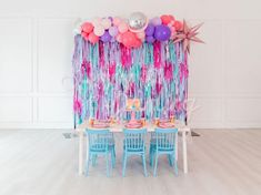 a party table set up with balloons and streamers on the wall, along with blue chairs