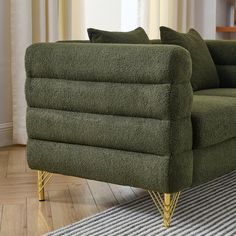 a green couch sitting on top of a wooden floor next to a rug and window