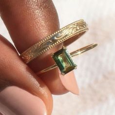 a woman's hand holding two gold rings with an emerald stone