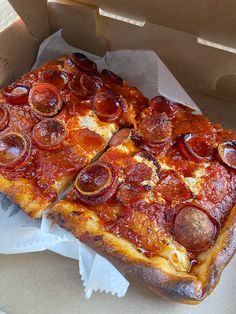 two slices of pepperoni pizza sitting in a box on top of wax paper and napkins