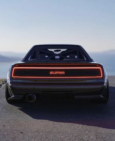 the rear end of a black sports car parked on top of a hill next to water