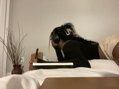 a woman laying in bed wearing headphones and writing on a book with a pen