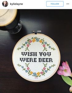 a cross stitch hoop with the words wish you were beer on it next to a pink flower