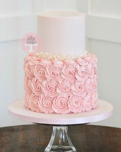 a pink cake with white frosting and roses on top is sitting on a table