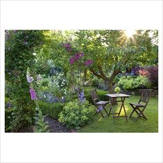 a table and chairs in the middle of a garden with purple flowers on the trees