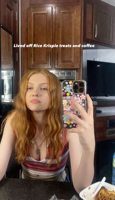 a woman taking a selfie in the kitchen with her phone and food on the counter