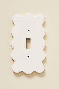 a white scalloped light switch plate on a beige wall with a black dot in the center