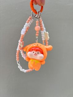 an orange monkey keychain hanging from a hook on a gray wall with white beads