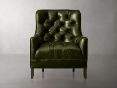 a green leather chair sitting on top of a cement floor next to a white wall