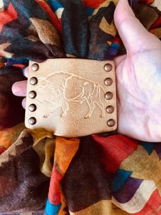 a hand holding a brown leather wallet on top of a colorful blanket