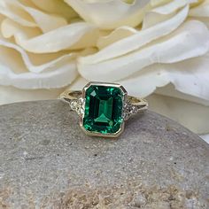 "The ring pictured is lab created emerald with moissanite accents #6974 -Approximate total carat weight: approx. 3.67ctw diamond equivalent -Center Stone Size: 10x8mm - approx. 3.55ct diamond equivalent -Center Stone Shape: emerald cut -Gem Type: lab created emerald -Stone Clarity: VS2 -Stone Color: green -Moh's Scale: 8.5 hardness -Side Stones Size: 6 round approx. 0.12ct. diamond equivalent -Gem Type: moissanite F VS2 -Metal Type and Purity: 14k yellow gold -Setting: half bezel design -Stock R Elegant Emerald Rings With Bezel Setting, Elegant 14k Gold Emerald Ring With Bezel Setting, Elegant Gold Emerald Ring With Smooth Bezel, Elegant Bezel-set Emerald Ring For May Birthstone, 14k Gold Bezel-set Emerald Ring, Blue Sapphire Studs, Emerald Ring Vintage, May Birthstone Rings, Bezel Set Ring