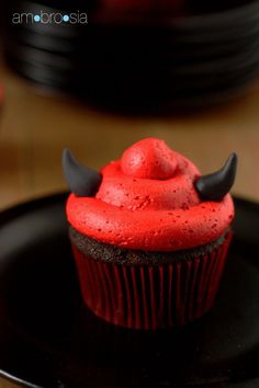 a cupcake with red frosting and black horns on it sitting on a plate