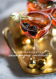 three glasses filled with drinks on top of a gold serving tray and garnished with herbs