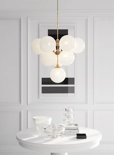 a white dining room table with glass bowls on it and a chandelier hanging from the ceiling