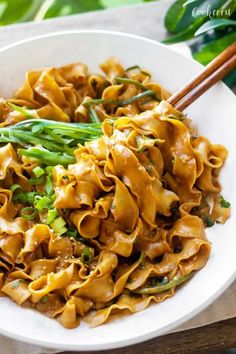 a white bowl filled with pasta and asparagus on top of a wooden table