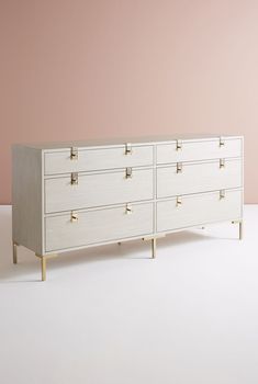 a white dresser with gold handles against a pink wall