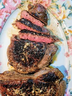 some steaks are on a white plate with pink flowers