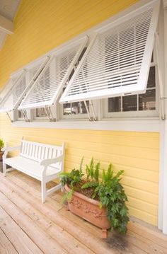 a white bench sitting on top of a wooden floor next to a yellow wall and planters