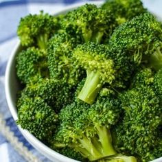 a white bowl filled with broccoli on top of a blue and white table cloth