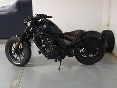 a black motorcycle parked next to a white wall in a room with concrete flooring