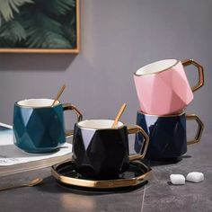 three coffee mugs with spoons on a table next to some books and other items