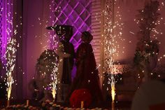 two people standing next to each other in front of a cake with sparklers on it