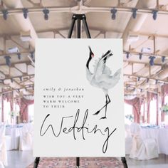 an easel with a wedding sign on it in front of a room filled with tables and chairs