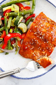 a white plate topped with salmon and veggies next to a fork on top of a table