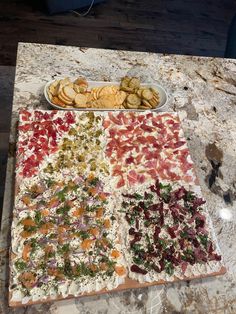 a platter of crackers and vegetables on a marble counter top next to a plate of chips