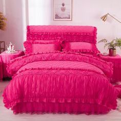 pink bedding with ruffles and pillows in a white room next to a potted plant