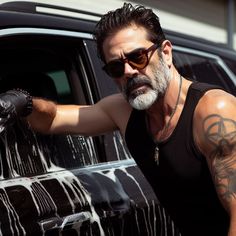 a man in sunglasses leaning on the door of a black car with his arm extended